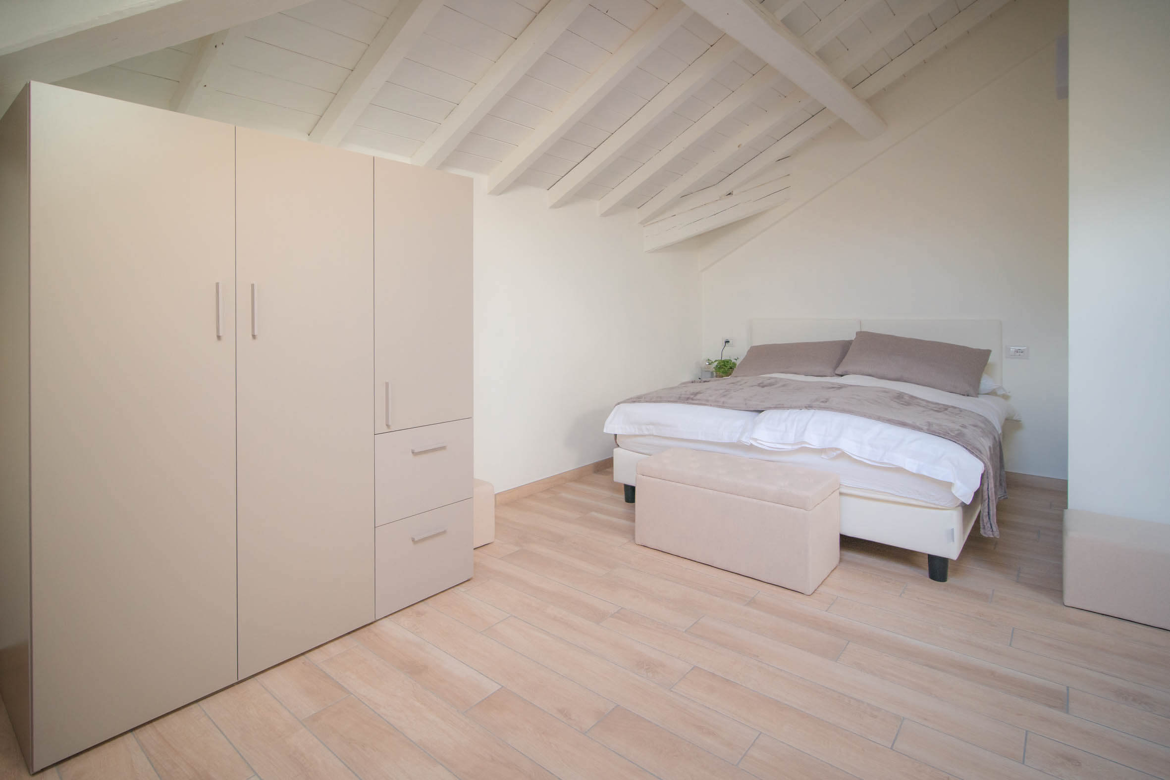 Camera da letto con letto, poltroncina, armadio e tetto con travi a vista