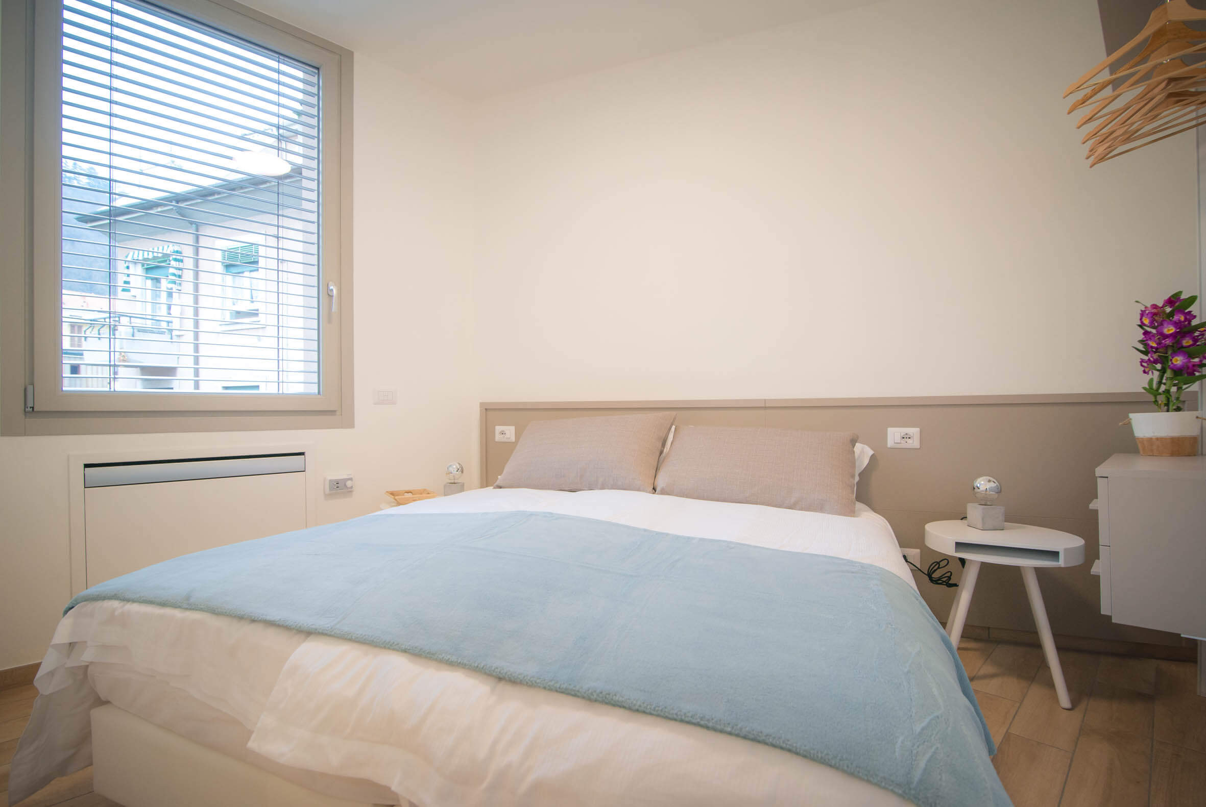 camera da letto con armadio con grucce a vista, lampada, comodini con piccole abat-jour e finesrta