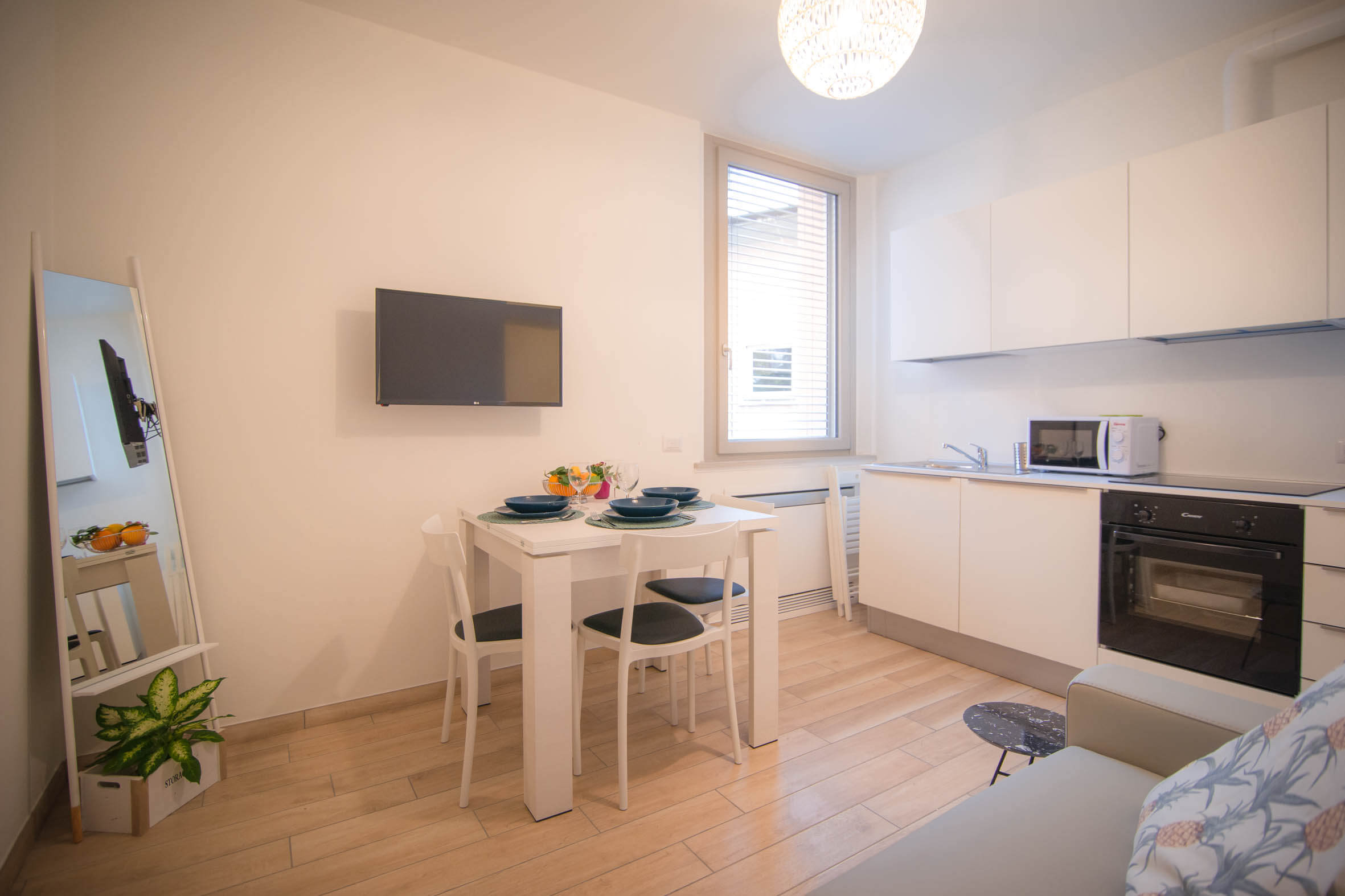 sala da pranzo con cucina attrezzata divano, tavolo con sedie, piatti e bicchieri ed elementi decorativi e finestra