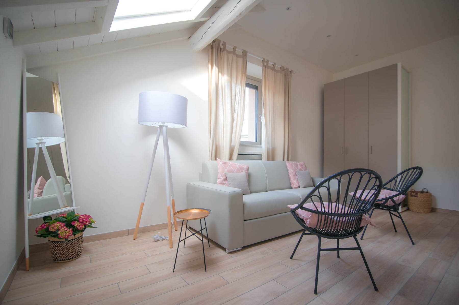 salotto con divano grigio, due sedie, armadio, lampada, specchio e piante decorative